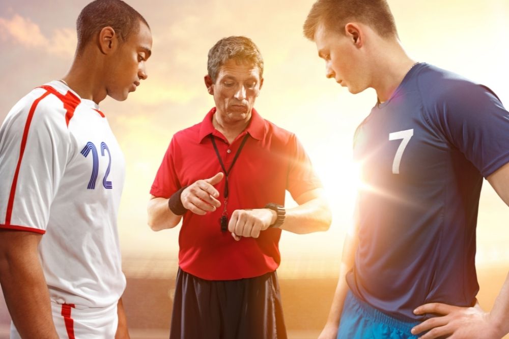 two soccer players and a referee is looking at the watch