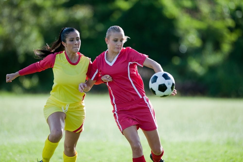 2 female soccer players use their elbows to gain an advantage in the ball situation