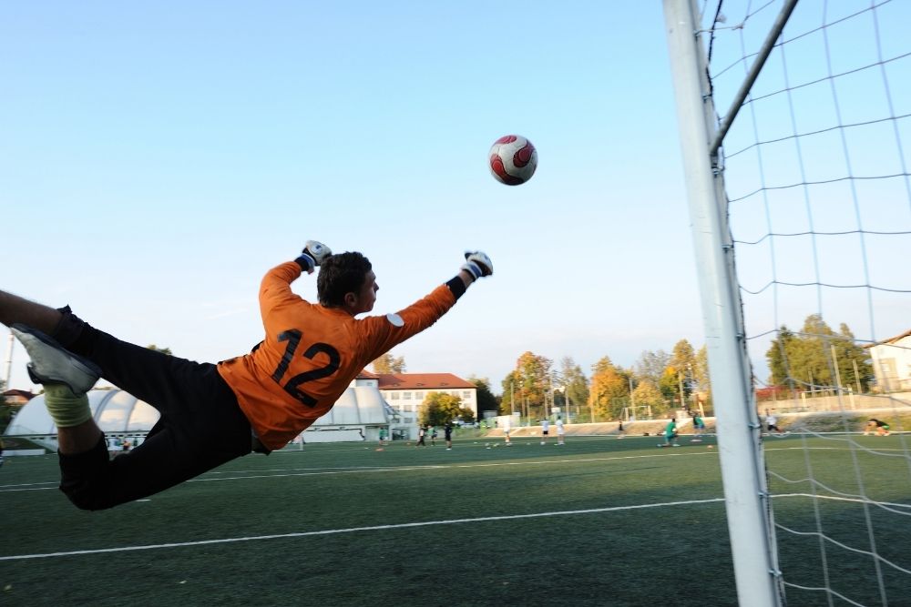 A goalkeeper is flying to stop the ball