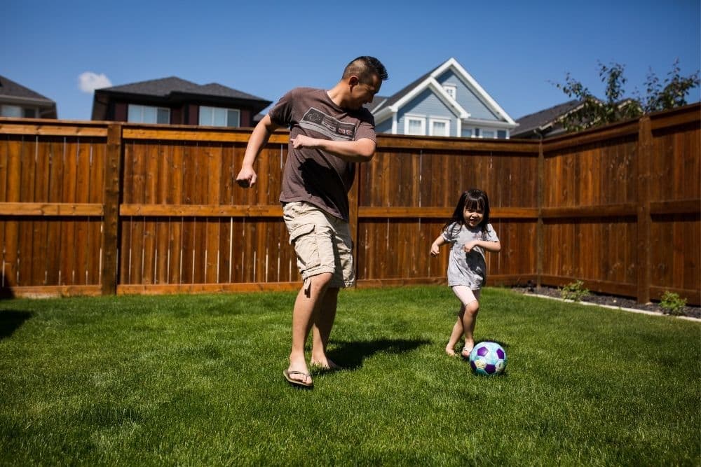 The man and his daughter are playing soccer in the garden