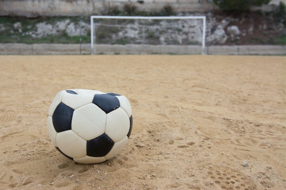 A deflated soccer ball is on the sand field