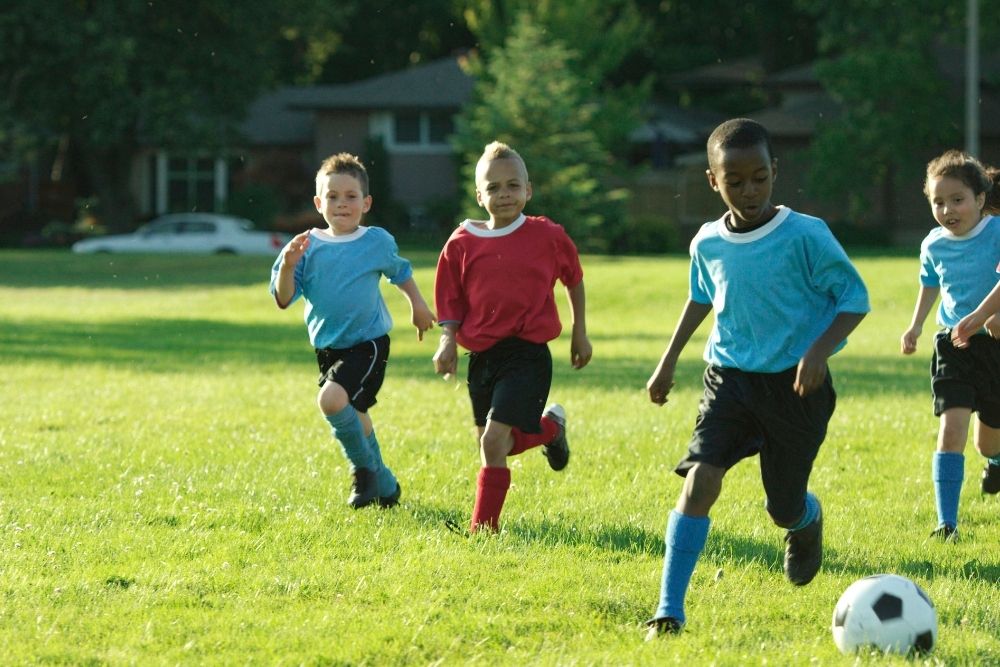 A kid player is dribbling the ball and the others are chasing him