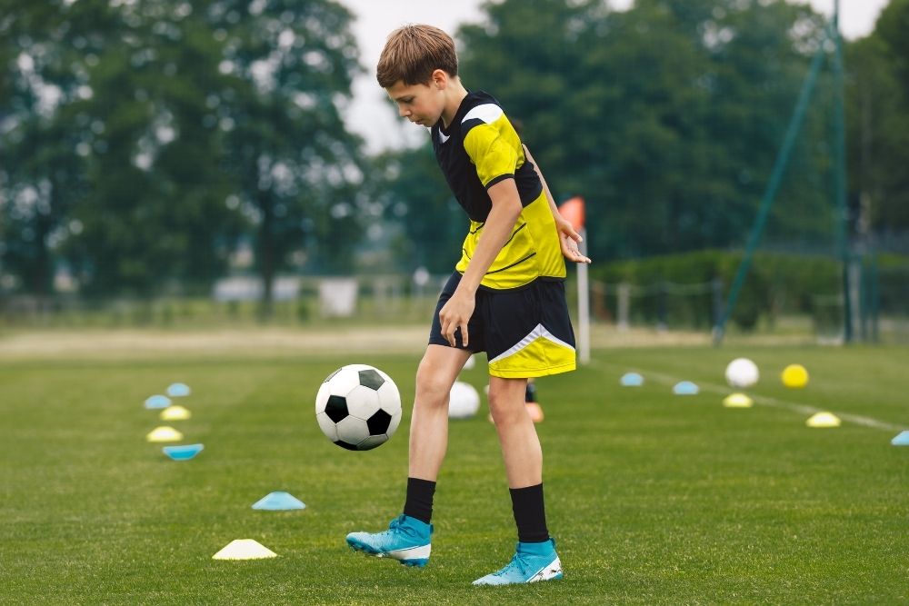 A kid soccer player is practicing ball juggling