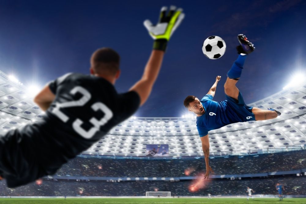 The player in black is kicking the ball with a difficult position and the goalkeeper has to fly to block the ball