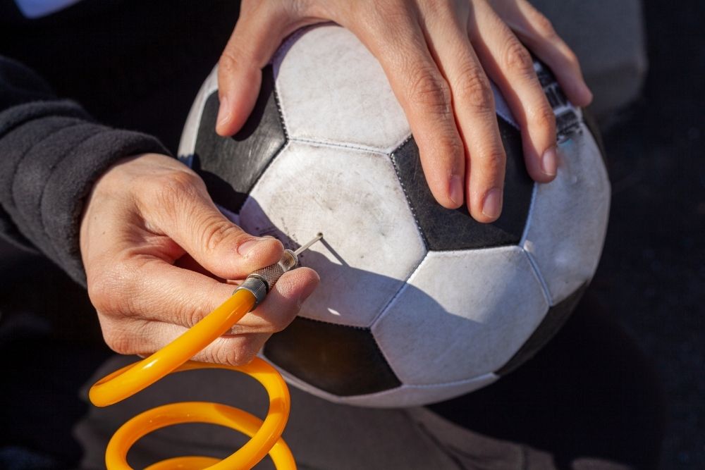 the person is trying to remove a needle from a soccer ball