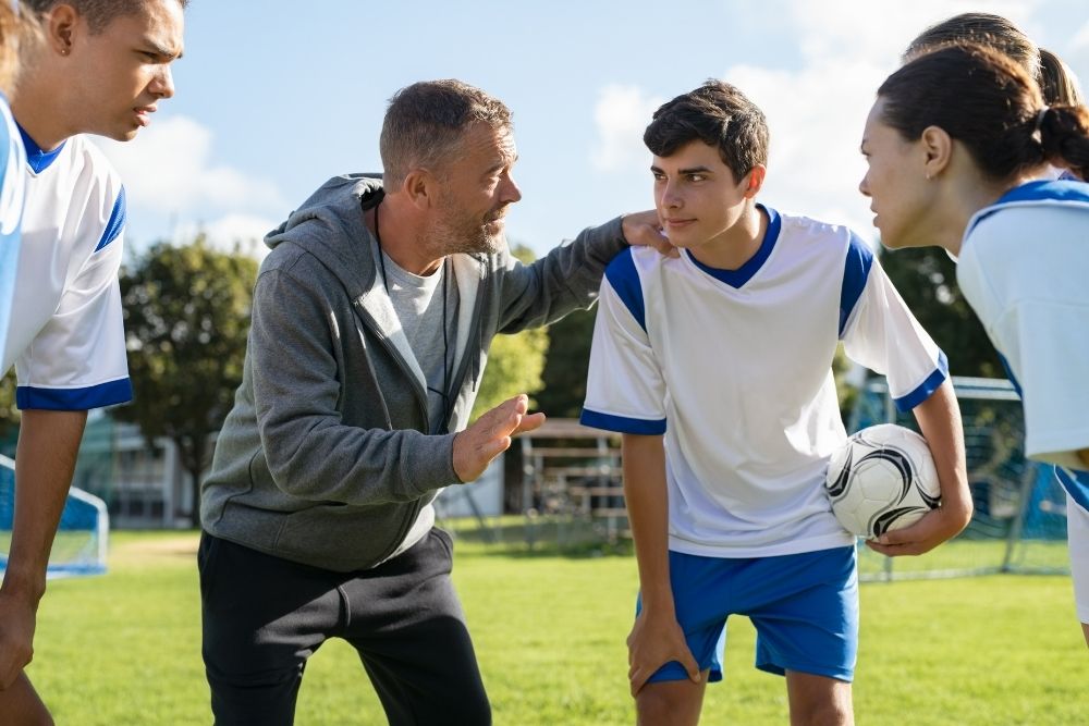 A coach and his players are discussing the tactic before a college soccer match
