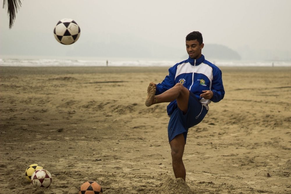 A soccer player is practicing on the beach