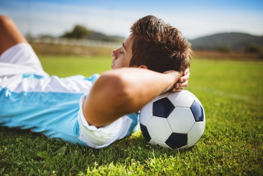 The player is resting his head on the soccer ball