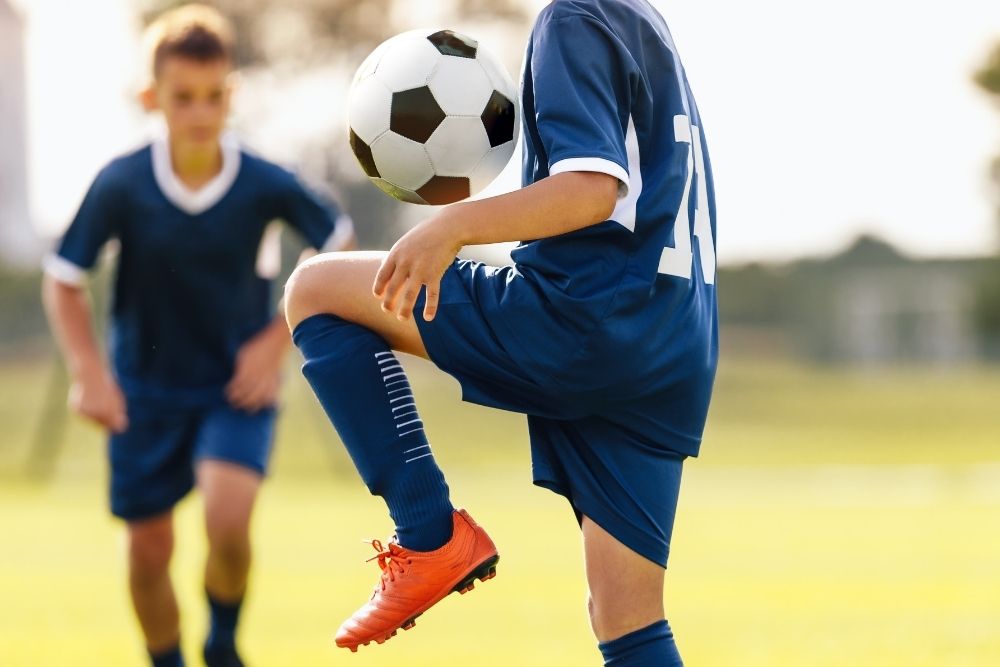 a kid keeps soccer ball in the air with his thigh