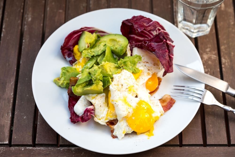 a plate of food consisting of eggs, avocados, and vegetables