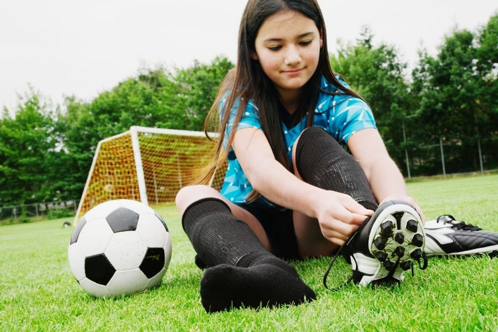 a girl sitting next to a soccer ball and taking off soccer cleats