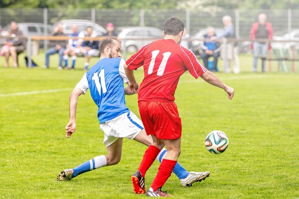 Blue soccer player try to block the ball for the red one