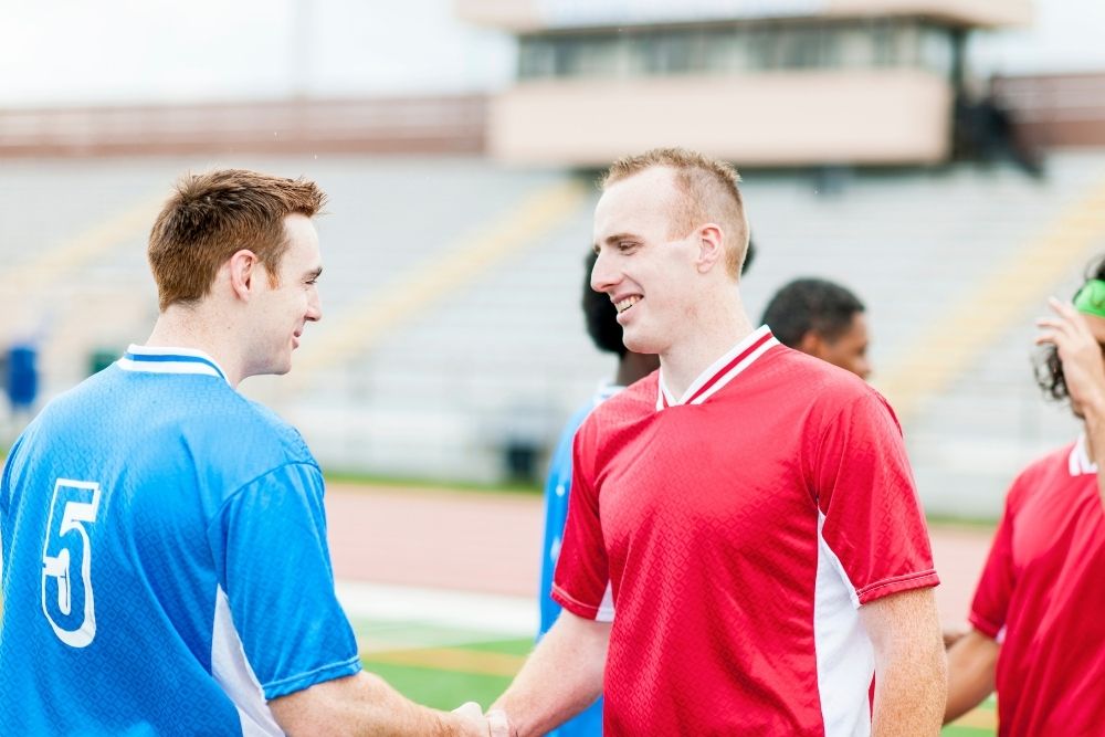 a fit soccer player is shaking hand with another player
