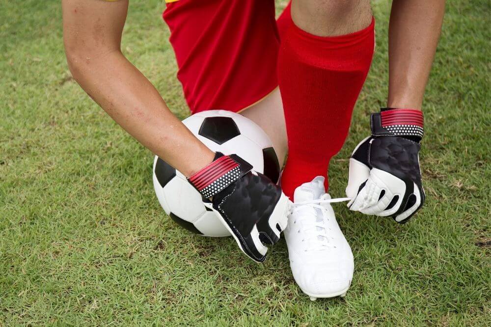 a soccer player wearing red socks and gloves tying shoelaces