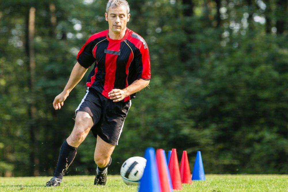 man wears black soccer shorts dribbling a soccer ball between cones