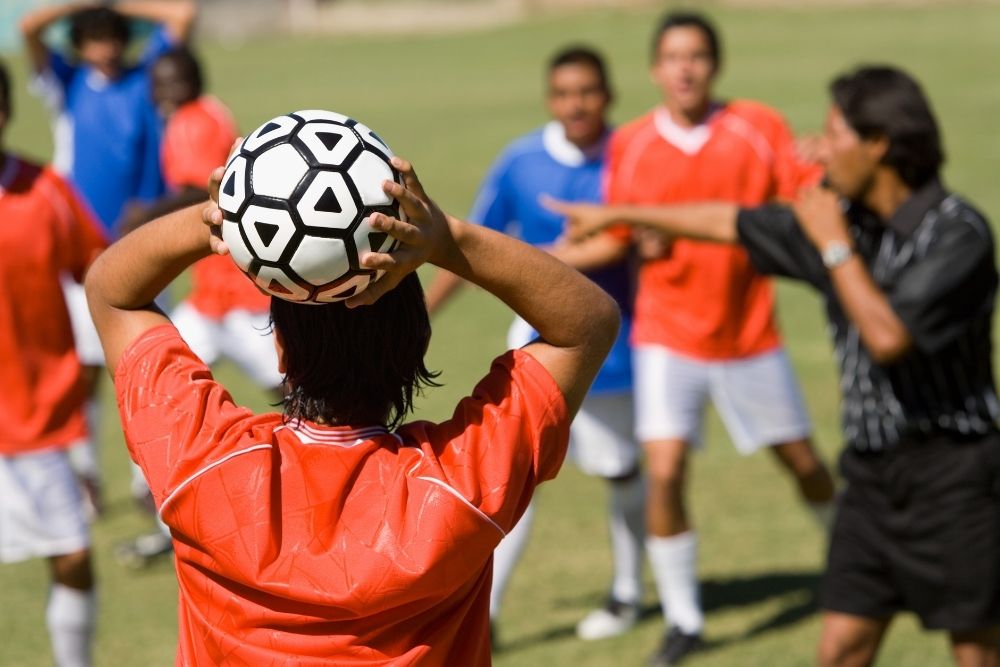 soccer player raises hand and holds the two sides of soccer ball behind his head to make a throw in