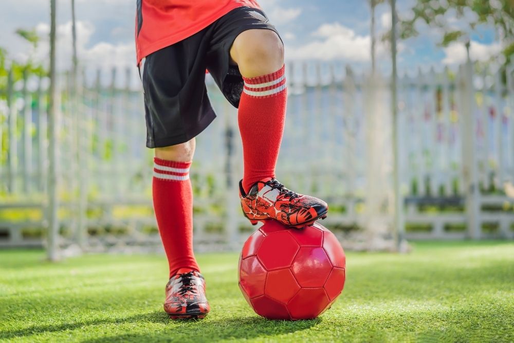 soccer player wears red socks with one leg putting on the red soccer ball