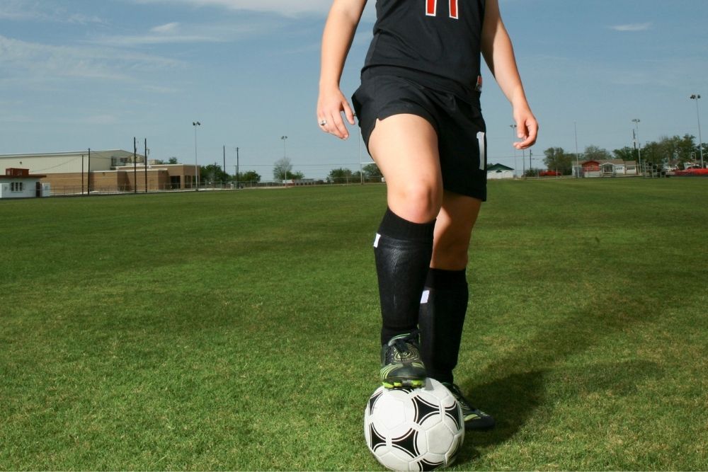 girl wearing black soccer socks with her soccer cleats on grass
