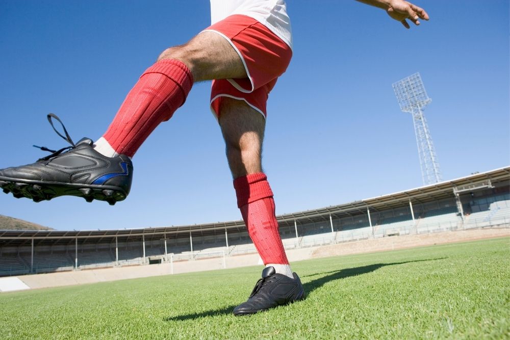 man wearing long red socks with black soccer cleats kicking his left leg