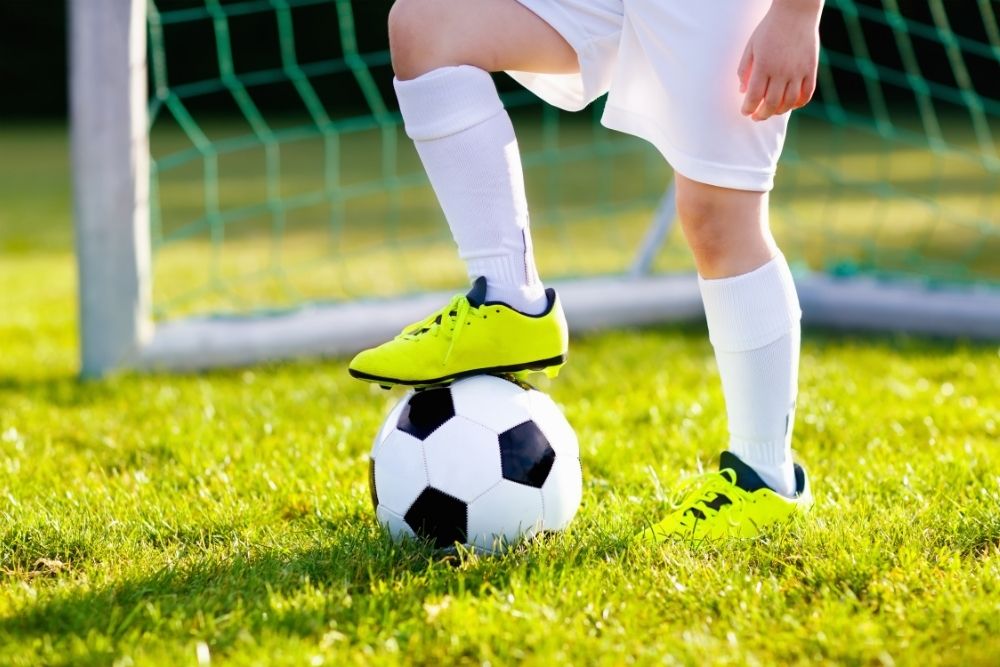 man wearing neon green soccer cleats putting on foot on soccer ball