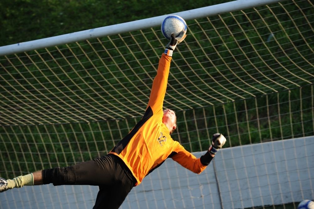 soccer goalie in orange jersey dives and hops to catch soccer ball