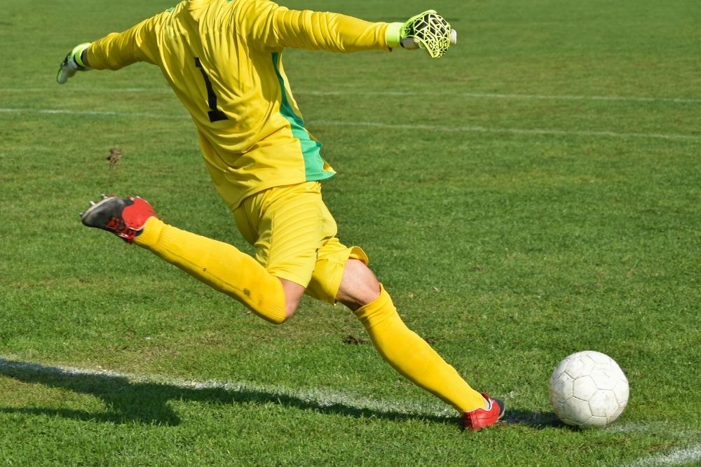 soccer goalie in yellow uniform kicking a ball