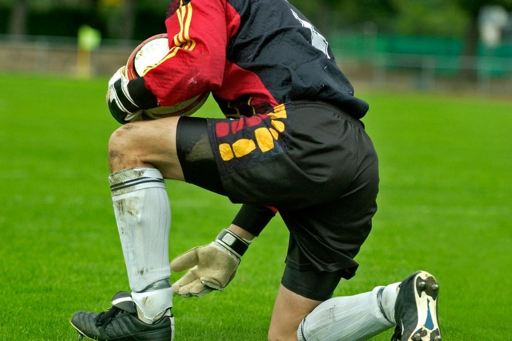 soccer goalkeeper taking a knee and holding a soccer ball in his arm