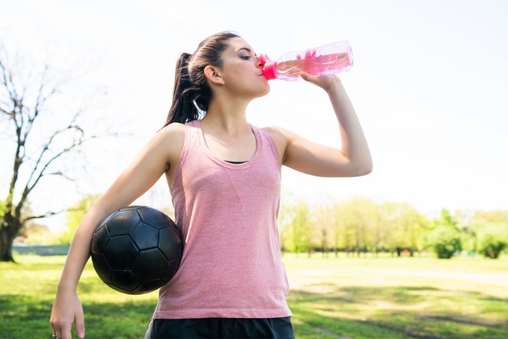 a girl drinking water while playing soccer