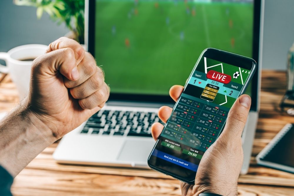 man follows a soccer match via his phone and laptop