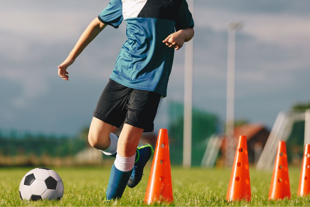 Soccer player are dribbling the ball through the cones