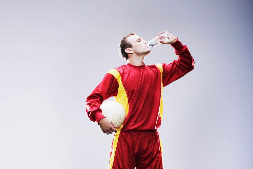 Soccer player is drinking water and are holding the soccer ball
