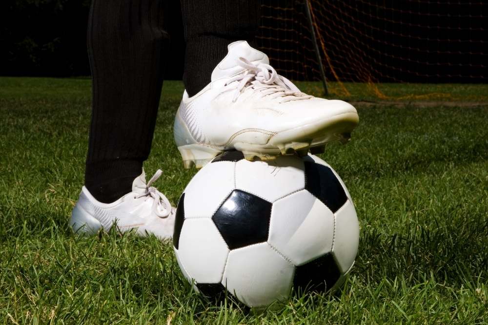 man places his white soccer cleats on the ball